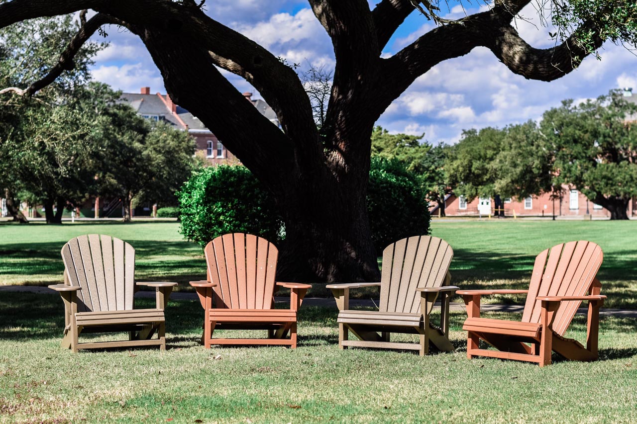 durable, sustainable, well-built outdoor Adirondack chairs sit on a lawn beneath a large tree in Texas.
