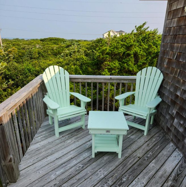 A pair of teal Adirondack chairs on a weathered porch with a side table