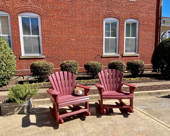 Red Adirondack rocking chairs matching the brick wall they are set against